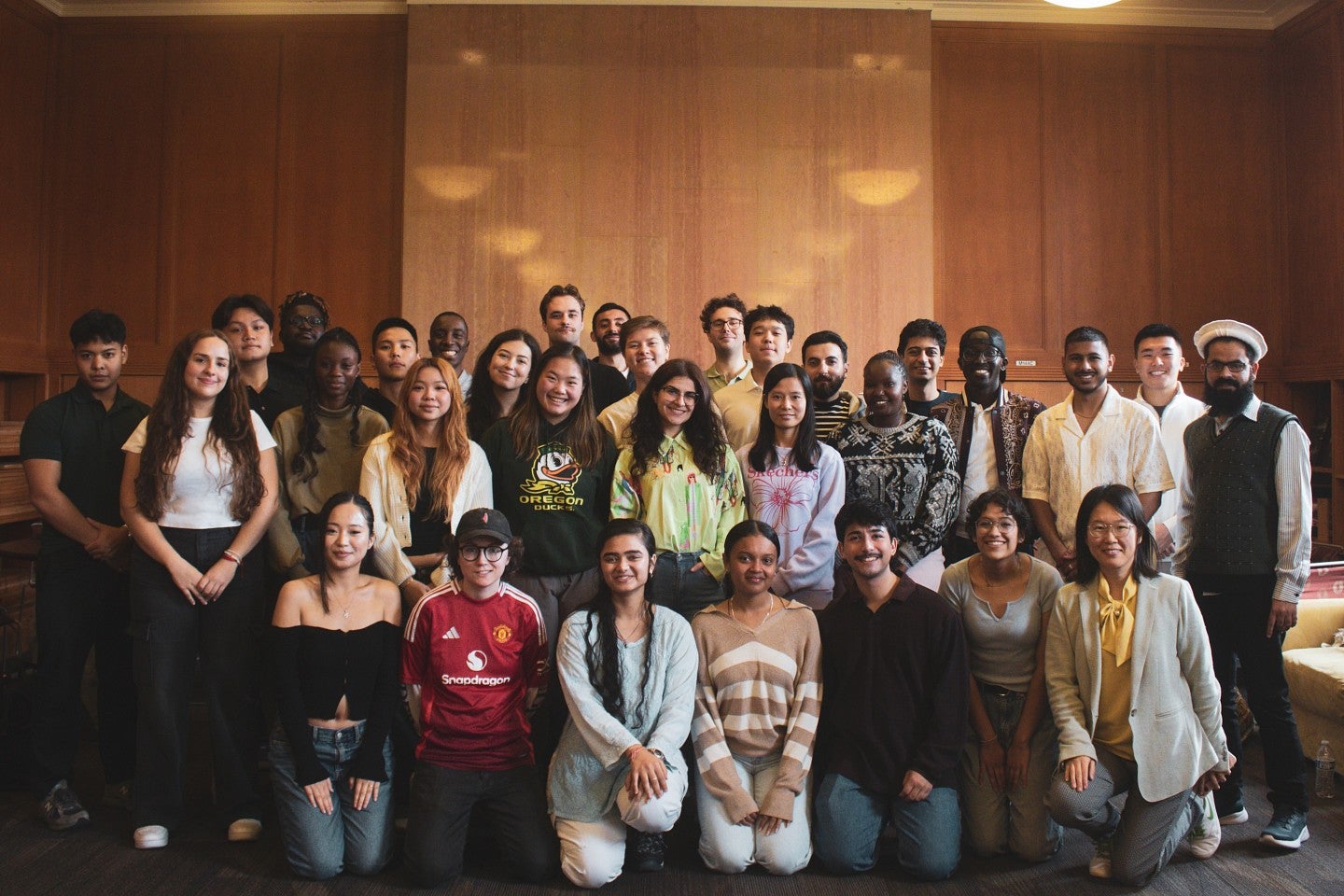 Group of international students posing for a photo in a room with wooden paneling on the walls