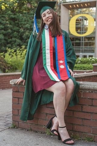 Student sitting in front of Lillis Hall in graduation cap