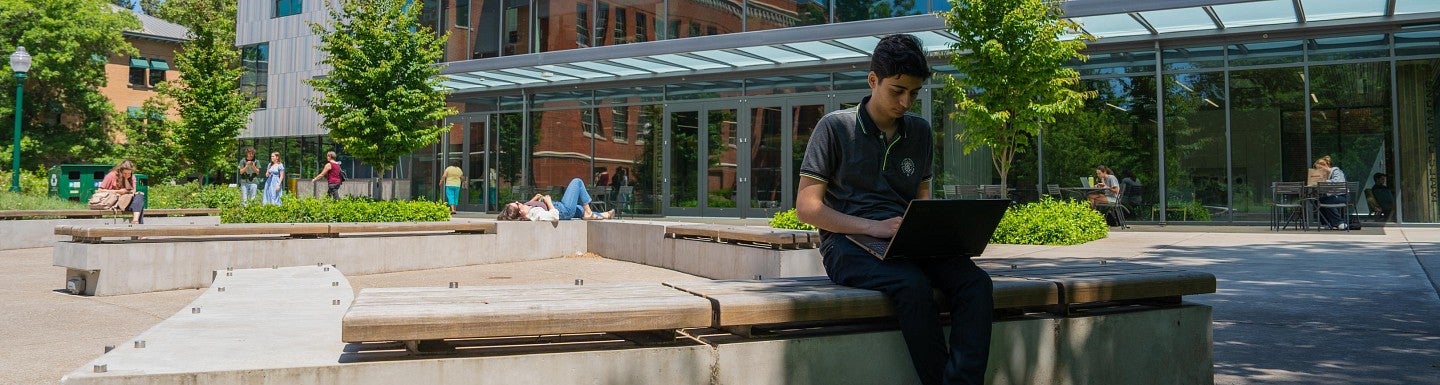 UO student sitting on a bench working on a computer