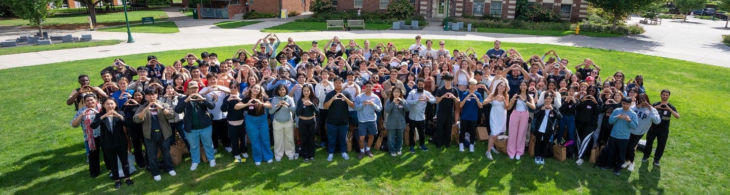 Large group of University of Oregon students standing on a lawn outsite holding up the "o" hand sign. 