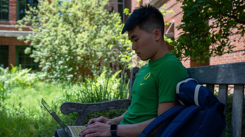 Male student sitting bench with laptop