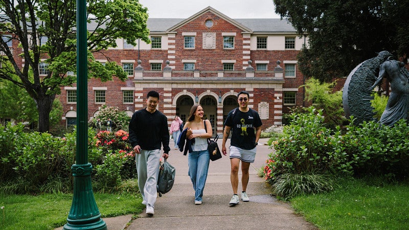 three international college students walking in front of a brick building