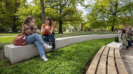 Students sitting on a small concrete wall eating a snack and conversing