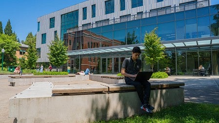 UO student sitting on a bench working on a computer