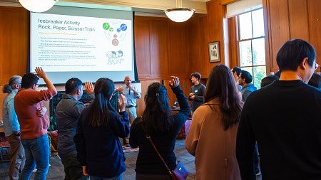 A group of college students actively engaging in a workshop, with several participants raising their hands to take part in an activity.