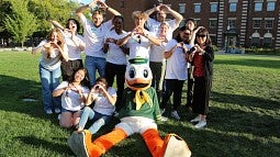 Group of students posing for a photo with the Oregon duck mascot holding up the "O" hand sign