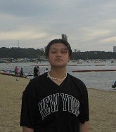 College-aged male standing on a beach wearing a black "New York" top. 