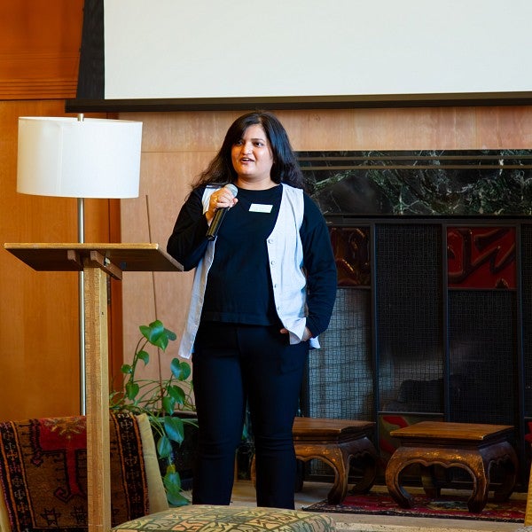 An international student holding a microphone while standing next to a podium